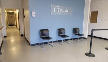 Interior waiting room with blue accent wall, BAART Programs logo, black seating chairs, and clean facility signage